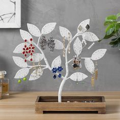 a white tree with earrings hanging from it's branches on a table next to a potted plant