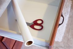 a pair of red scissors sitting on top of a white table next to a roll of paper