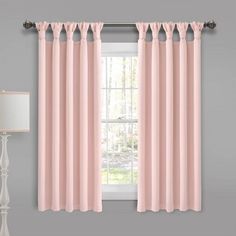 pink curtains hanging on the side of a window in front of a lamp and table