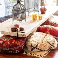 a bird cage sitting on top of a wooden table next to pillows and rugs