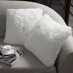 a white couch with two pillows and a cup on it next to a coffee mug