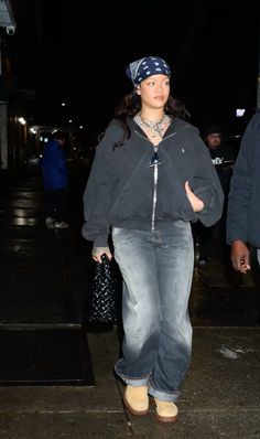 a woman with a bandana on her head is walking down the street at night