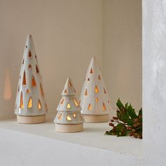 three white candles sitting on top of a shelf next to a pine cone candle holder