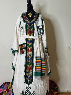 Ethiopian and Eritrean traditional dress (habesh kemis gonder kemis)garment featuring colorful and intricate embroidery. This style is often seen in Ethiopian or Eritrean cultural clothing, known as "Habesha kemis." The dress is typically worn by women for special occasions and celebrations. The garment in   likely  white cotton or linen and adorned with detailed patterns along the neckline, cuffs, and front panel, reflecting the rich textile heritage of the region. Festive Habesha Kemis With Traditional Patterns, Habesha Kemis For Traditional Ceremonies During Eid, Habesha Kemis For Eid With Traditional Patterns, Eid Habesha Kemis For Traditional Ceremonies, Ceremonial Habesha Kemis For Eid With Traditional Patterns, Traditional Habesha Kemis For Ceremonial Occasions, Ceremonial Habesha Kemis With Traditional Patterns, Traditional Habesha Kemis For Ceremonies, Festive Habesha Kemis For Traditional Ceremonies