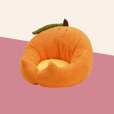 an orange shaped pillow with a smiling face on it's side and a green leaf sticking out of its top