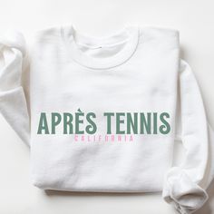 Après Tennis Sweatshirt I love to help my customers with custom orders, if you have a specific request (adding team or club name, bachelorette party personalization, a different sweatshirt color, design on a shirt, or a swap to a Comfort Colors sweatshirt), please message me and I will promptly get back to you! This is a Gildan Sweatshirt with a UNISEX FIT. Please review the size chart in the images before you place your order. If you have any questions about sizing, I would be happy to help! If you don't see the specific color that you are looking for, please message me and I will get back to you quickly. If you are looking for a women's fit sweatshirt, please message me! PRODUCTION and SHIPPING Production takes about 1-3 days and standard shipping is 3-5 business days. If you are in a ru Crew Neck Top With Screen Print For Sports Events, Screen Print Crew Top For Sports Events, Screen Print Crew Neck Top For Sports Events, Sports Season Branding Crew Neck Sweatshirt, Sports Season Crew Neck Sweatshirt With Branding, White Fan Apparel Sweatshirt For Team Events, Branded Crew Neck Top For College, Crew Neck Sweatshirt For Sports Season, White Crew Neck Top For Team Events