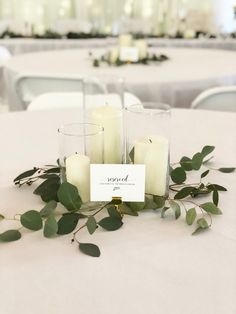 candles are sitting on top of a table with greenery and place cards in front of them