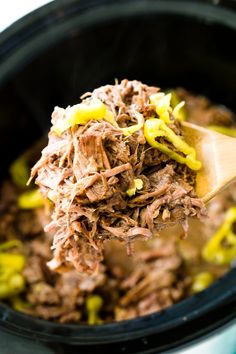 a wooden spoon full of shredded meat in a slow cooker