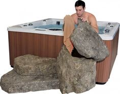 a man sitting in a hot tub next to two large rocks