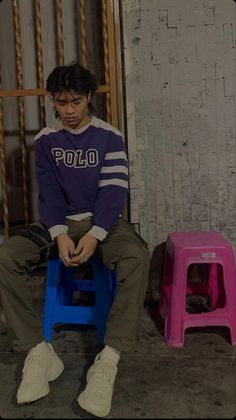 a young man sitting on top of a blue chair next to a pink and purple stool