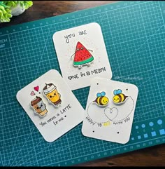 three magnets with different designs on them sitting on a cutting board next to a potted plant