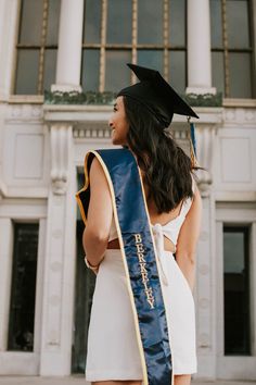 a woman wearing a graduation gown and holding a blue sash in front of a building