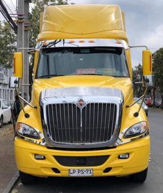 a yellow semi truck parked on the side of the road next to a traffic light