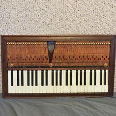 an old wooden piano sitting on top of a bed next to a gray sheet covered wall