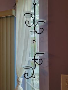 an iron candle holder in front of a window with white curtains and drapes on the windowsill