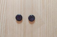 two small black buttons sitting on top of a wooden table next to each other with purple and blue speckles