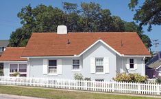 a white house with red tile roof next to a white picket fence