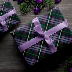 two wrapped presents sitting on top of a wooden table next to christmas tree branches and purple ornaments