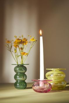 a lit candle sitting on top of a table next to two vases filled with flowers