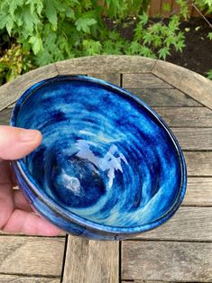 a hand holding a blue bowl on top of a wooden table