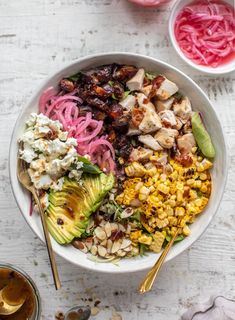 a bowl filled with chicken, avocado, and other vegetables next to two bowls of dressing