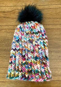 a multicolored knitted hat with a black pom - pom on top