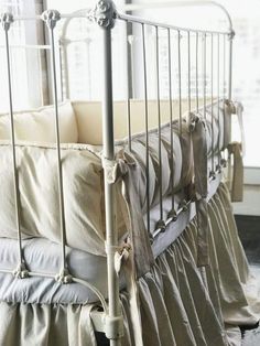 a metal crib with ruffles and pillows on the bottom row, in front of a window