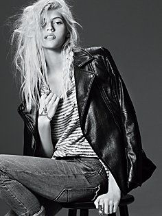 a woman sitting on top of a stool next to a black and white photo with her hair blowing in the wind