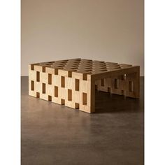 a wooden bench made out of squares on top of a cement floor in front of a wall