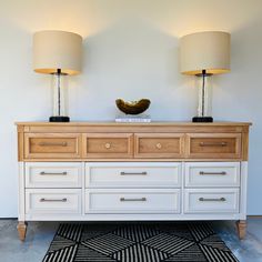 two lamps sitting on top of a white dresser next to a black and white rug