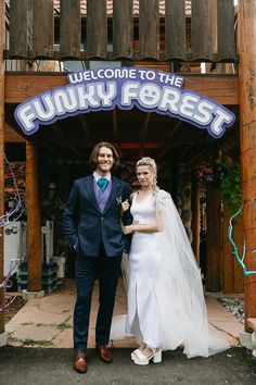 a bride and groom standing in front of the funky forest sign