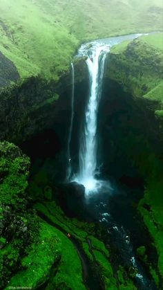 a large waterfall in the middle of a lush green mountain range with water running down it's sides