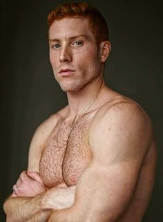 a man with red hair and no shirt is posing for the camera, his arms are crossed