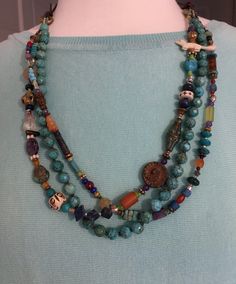 "Southwestern necklace that stars with jeans or silk. One strand is beautiful, hand-knotted faceted turquoise. The additional strands are filled with African trade beads, animals, flowers and a Willendorf female figure. Amethyst, carnelian, lapis and carved bone. Two moving manipulative features. Adjustable from 16\" to 39\"." Bohemian Double Strand Beaded Necklaces With Gemstones, Bohemian Double Strand Gemstone Beaded Necklaces, Bohemian Double Strand Gemstone Beaded Necklace, Southwestern Multi-strand Beads For Jewelry Making, Bohemian Hand-strung Blue Beads, Bohemian Blue Natural Stones Beads, Blue Bohemian Natural Stones Beads, Southwestern Multi-strand Gemstone Bead Necklaces, Southwestern Multi-strand Necklace With Gemstone Beads