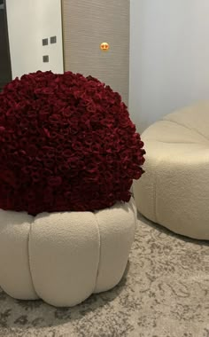 a large white vase with red flowers in it on a counter top next to two round stools