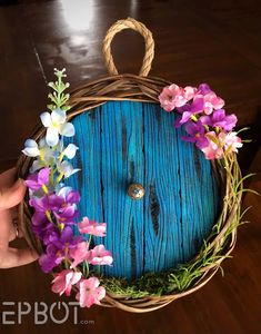 a hand holding a blue door with flowers on the front and side, surrounded by greenery