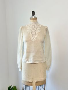 1970s Gunne Sax sheer cotton ivory long sleeve blouse with button down closure down the back middle. This shirt has a gorgeous floral lace mock neck that continues down the front middle.  In very good vintage condition, minor discoloration by armpit it hardly noticeable! B: 34" W: 31" L: 22" Vintage Beige Blouse For Spring, Fitted Off White Long Sleeve Blouse, Fitted Off White Blouse With Long Sleeves, Vintage White Blouse For Spring, Cream Long Sleeve Sheer Top, Long Sleeve Sheer Cream Top, 1970s Long Sleeve Blouse, Vintage Cream Blouse, Vintage Beige Cotton Blouse