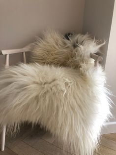 a white furry chair sitting on top of a hard wood floor next to a wall