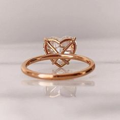 a gold ring with a heart shaped diamond on it's side, sitting on a white surface