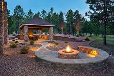 an outdoor fire pit surrounded by rocks and trees at night with lights on the patio