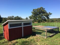 a chicken coop in the middle of a field with a red shed and white roof