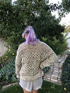 a woman with purple hair is standing in front of an apple tree wearing a crocheted sweater