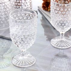 three glass goblets sitting on top of a table next to pine cones and napkins