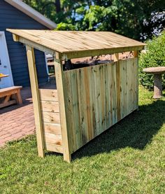 a wooden storage shed sitting on top of a lush green field next to a picnic table