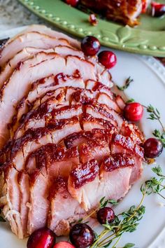 sliced ham with cranberry sauce on a white plate next to fresh cherries