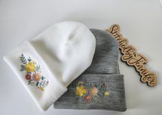 two hats with embroidered flowers on them next to a wooden name sign that says welcome home