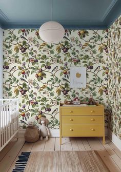 a baby's room with floral wallpaper and yellow dresser in the foreground