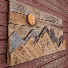 a wooden wall hanging on the side of a building with mountains and a round object