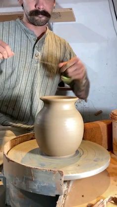 a man is making a vase on a potter's wheel with one hand and the other holding something in his other hand