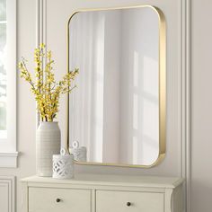 a vase with yellow flowers sitting on top of a white dresser next to a mirror